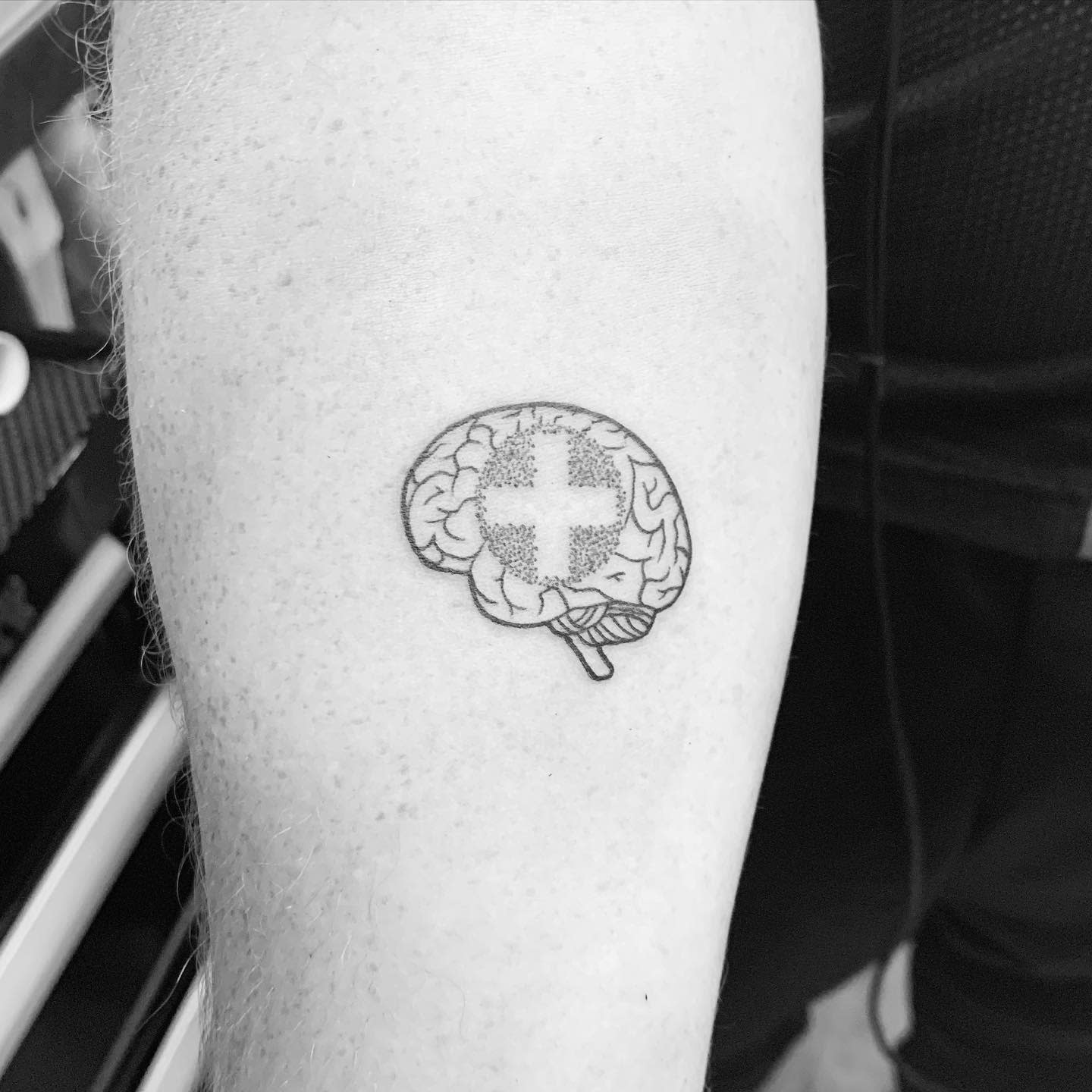 Tattoo of a brain with a cross symbol on an arm